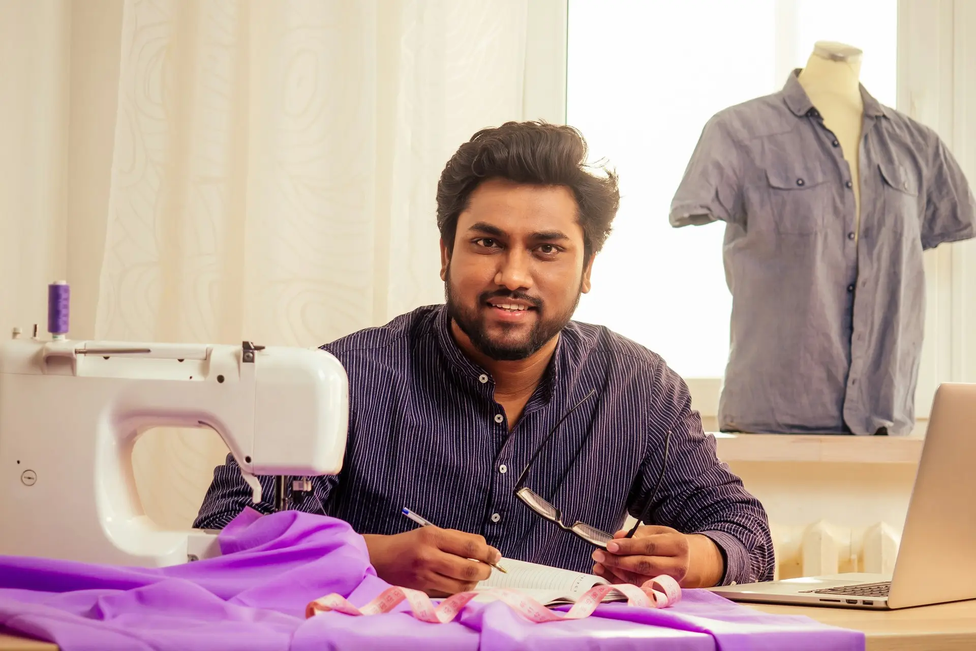 handsome indian tailor man In a stylish shirt workinh with violet cotton textile